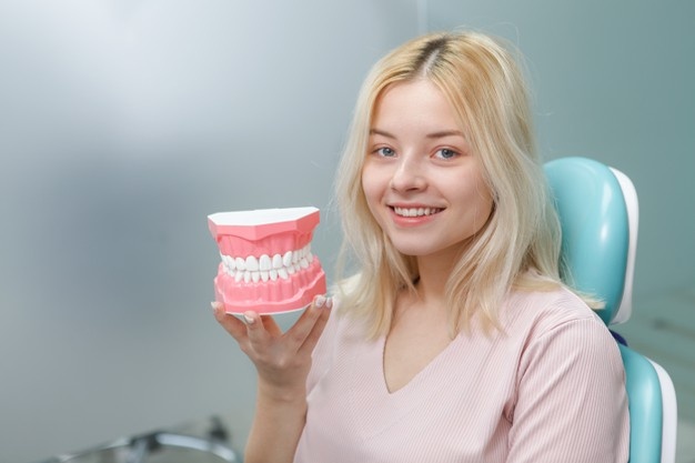 happy-young-woman-with-white-healthy-teeth-holding-jaw-model-sitting-dental-chair_118628-2784